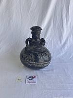 Front view of black ceramic vessel with sculptural figure and incised motifs