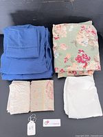 Stacked blue sheets, green floral sheet, beige paisley and off-white pillow covers