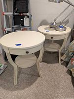 Pair of round cream distressed wood end tables displayed side by side