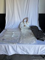 All lot items laid out: stack of clear Space Bag storage bags, white Cozy Earth tote, folded black garment bag