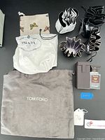 Group shot of all items including bottle, travel case, TOM FORD dust bag, PRADA dust bag, butterfly pouch, and several drawstring pouches