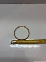 Bangle laid flat beside measuring tape showing 2.25 in inner diameter