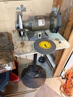 Bench grinder mounted on pedestal with loose extra wheel on table