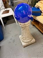 Blue glass gazing ball resting on ornate off-white resin pedestal