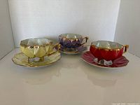 Front view of three coloured teacups with matching saucers