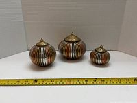Three graduated striped brass jars with lids, tape measure for scale