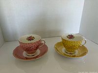 Pink and yellow Colclough teacup and saucer sets displayed side by side
