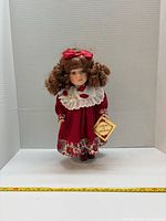 Full view of porcelain doll on stand with measuring tape for scale