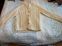 Full view of cream Aran knit cardigan laid flat showing front, sleeves, collar and toggle buttons