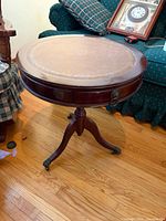 Full view of round mahogany side table showing leather top, pedestal base, casters