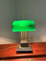 Front view of lamp showing green glass shade, brass columns, marble base