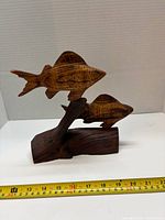 Front view of two-fish wood sculpture with measuring tape for scale