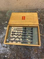 Open wood case showing six spiral auger bits seated inside