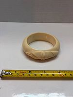 Top view of cream carved bangle with tape measure showing inner diameter