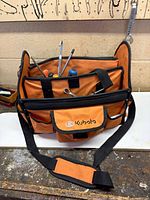 Kubota orange and black tool bag with visible screwdrivers, wrenches and assorted tools inside pockets