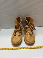 Front view of pair of tan ankle moccasin boots with laces and fringe