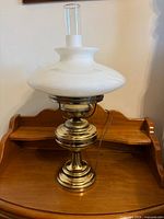 Full view of first brass hurricane lamp showing metal base, white glass shade and clear chimney