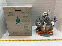 Haunted house tealight holder beside original box with measuring tape