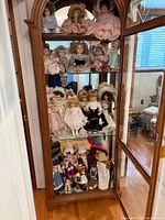 Full view of wooden curio cabinet filled with multiple porcelain Victorian style dolls on four shelves