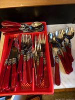 Flatware set arranged in red tray with additional spoons beside