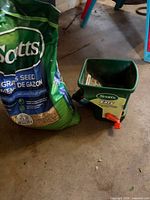 Bag of Scotts grass seed beside handheld spreader