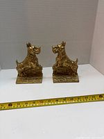 Both brass Scottie dog bookends with measuring tape showing size