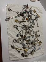 Full lot spread on cloth showing quantity and variety of souvenir spoons