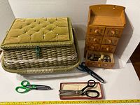 Wicker basket, wooden chest, scissors, measuring tape visible