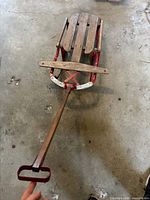Top view of sled showing wood slat deck, red metal frame, steering bar and pull handle