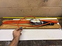 Full view of handheld work light wrapped on board, showing orange cord and plug