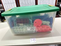 Clear plastic tote with green lid containing assorted silicone molds in multiple colors and shapes