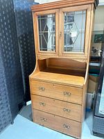 Full view of oak bureau showing leaded glass upper cabinet, drop-front surface, three drawers