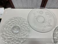 Top view of two pressed glass plates showing lattice/starburst design and relief cherub/floral design