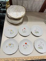Six floral dessert plates with embossed rims alongside stacked covered gravy dish