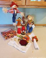 Group shot of scarecrows, spoon rest, napkin ring, cloth napkin, felt trivet, pumpkin accent and bag of leaves