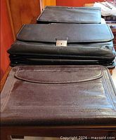 Three leather cases stacked: brown envelope holder, black fold-over briefcase, black zip-around padfolio