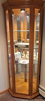 Full view of corner curio cabinet showing wood frame, glass panels and interior lighting