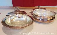 Both silver-plated serving bowls with lids open displaying glass inserts