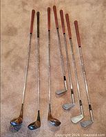 Six golf clubs laid out full length on carpet