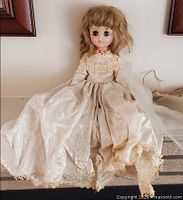 Front view of vintage doll seated wearing full ivory wedding gown