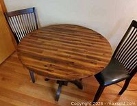 Round wooden table with both leaves raised, flanked by two chairs
