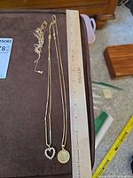 Three gold-tone necklaces laid beside 18-inch ruler for scale