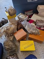 Multiple boxed and loose doll wigs beside storage bin; visible Monique and Kemper Originals boxes