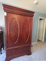 Closed armoire front showing cherry veneer, oval panels, lower drawer