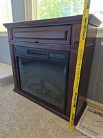 Front view of dark brown electric fireplace mantel with tape measure indicating height