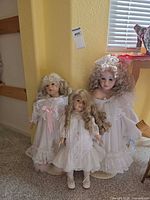 Front view of three porcelain dolls with stands against wall