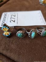Four silver rings lined on brown surface; includes multicolor inlay ring and three turquoise cabochon rings