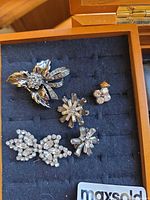Overview of five silver-tone rhinestone brooches in display box