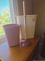 Pink small wastebasket, cream/off-white medium wastebasket, wood-handle plunger