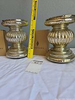 Front view of both ribbed mercury glass candle holders with tape measure for scale and Luminara boxes